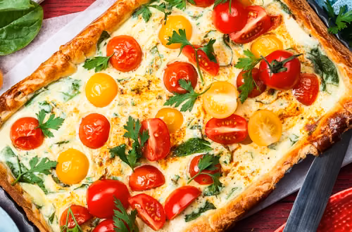 Masę jajeczną wylewam na ciasto francuskie, dorzucam pokruszony ser, pomidorki i rukolę! W 40 minut mam pyszną tarte
