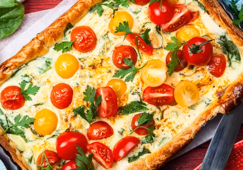 Masę jajeczną wylewam na ciasto francuskie, dorzucam pokruszony ser, pomidorki i rukolę! W 40 minut mam pyszną tarte